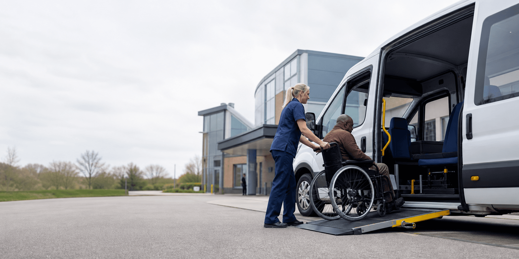 A patient transport professional assisting a wheelchair passenger into an accessible transport vehicle